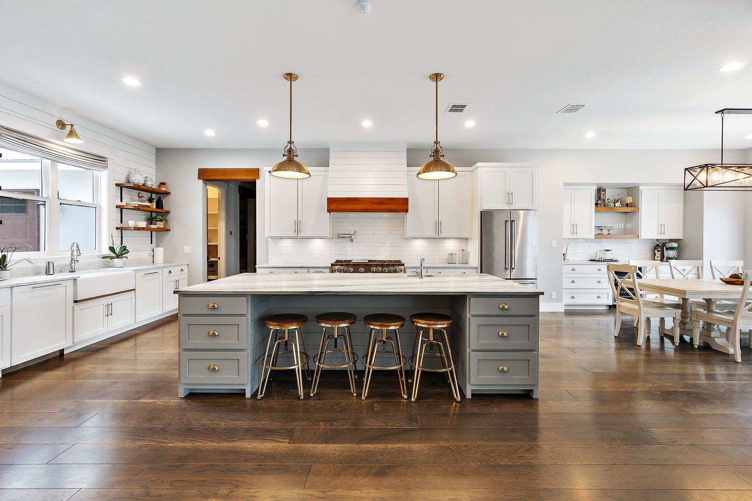 Open-concept kitchen with large marble island, brass pendants, and hardwood floors
